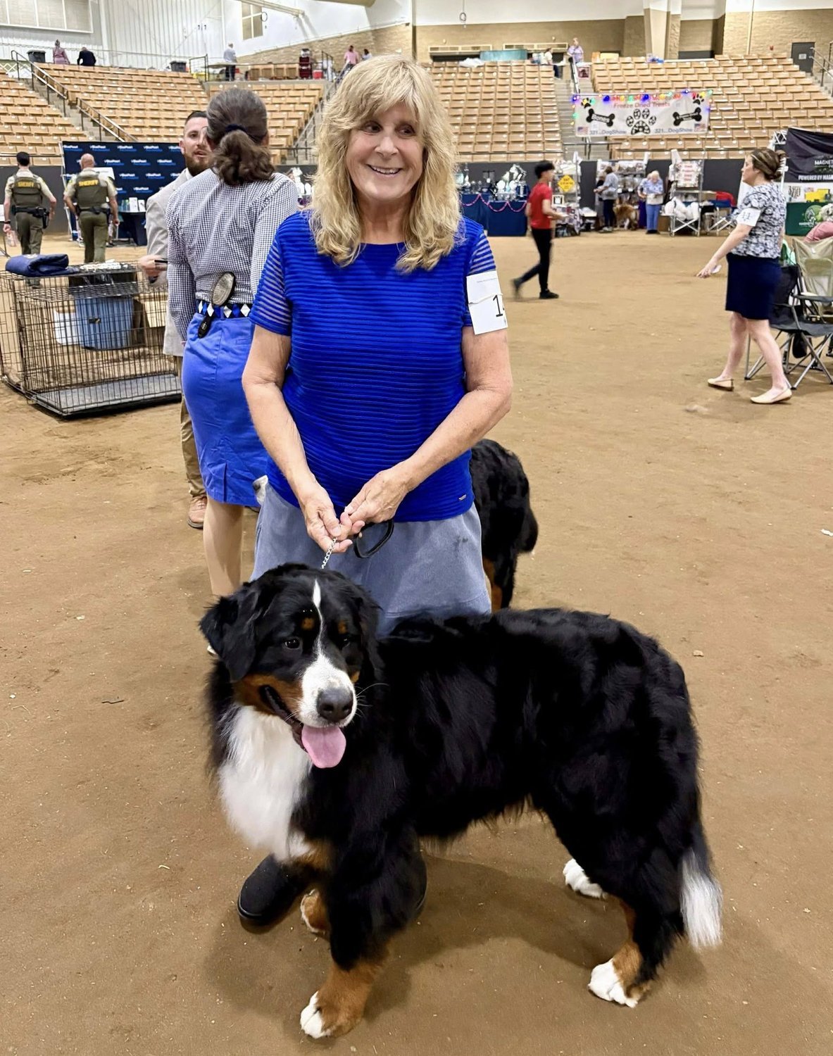 Cindy Loflin holding a winning ribbon with her Bernese Mountain Dog at an indoor dog show.